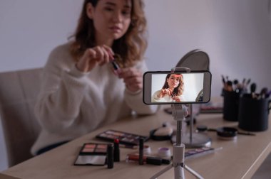 Kafkasyalı genç bir kadın cep telefonunda bir makyaj eğitimi videosu kaydediyor. Video blogcusu kız makyaj yapıyor.