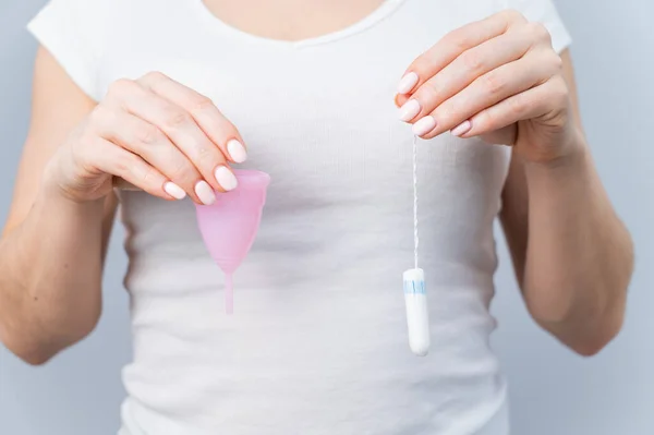 Close-up de uma mulher segurando um copo menstrual rosa e tampão contra um fundo branco — Fotografia de Stock
