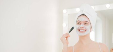 Saçında havlu olan güzel beyaz kadın kilden bir maske takıyor. Evdeki güzellikle ilgilenmek.