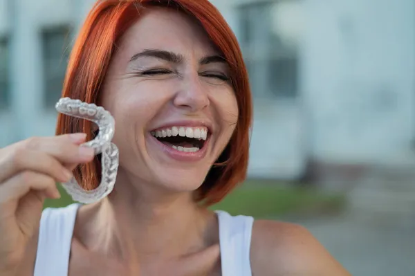 Femme blanche aux cheveux roux tenant des protège-dents transparents pour la correction des morsures à l'extérieur. Une fille avec un beau sourire blanc neige utilise des accolades en silicone — Photo