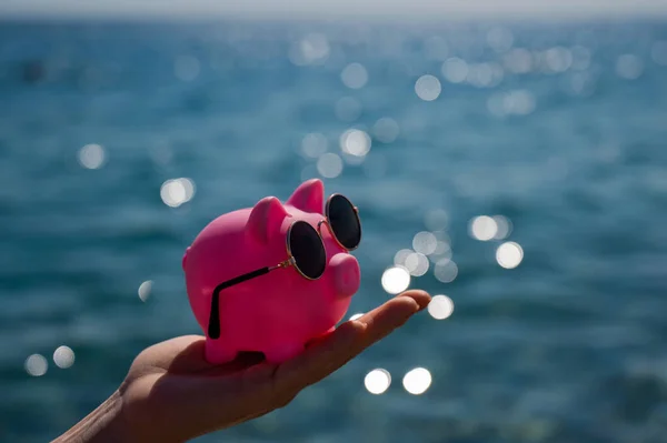Μια γυναίκα κρατά έναν κουμπαρά με γυαλιά ηλίου στο βάθος της θάλασσας. Δημοσιονομικές διακοπές. — Φωτογραφία Αρχείου