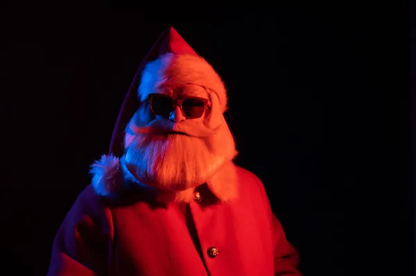 Babbo Natale in occhiali da sole in luce al neon su sfondo nero. Festa di Natale. — Foto Stock