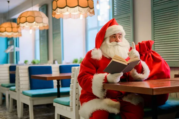 Papá Noel está sentado en un café y leyendo un libro — Foto de Stock