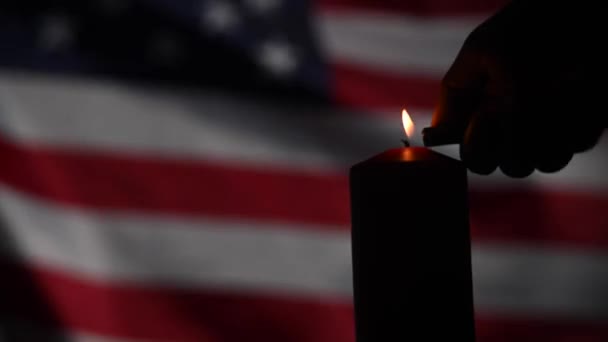 Um homem acende uma vela no fundo da bandeira acenando dos Estados Unidos da América no escuro. — Vídeo de Stock