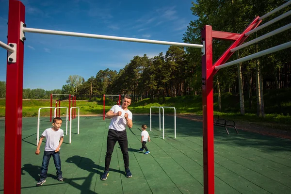 Uomo caucasico e due ragazzi che fanno esercizi all'aperto. Padre e figli si allenano sul campo sportivo — Foto Stock
