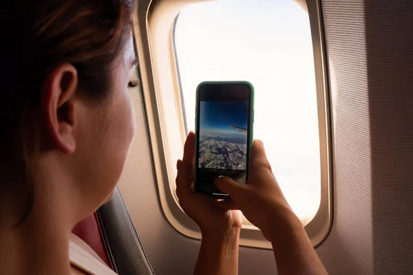 Mujer caucásica fotografías por teléfono inteligente el cielo en la ventana del avión. — Foto de Stock