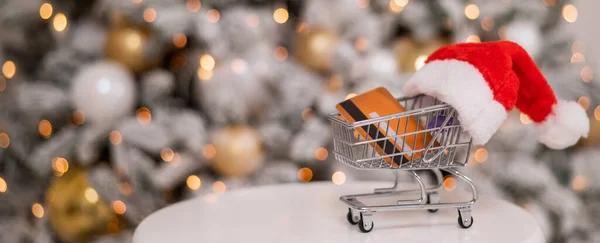 Presentes de Natal compras conceito. Cartão de crédito no carrinho de compras junto à árvore de natal. — Fotografia de Stock