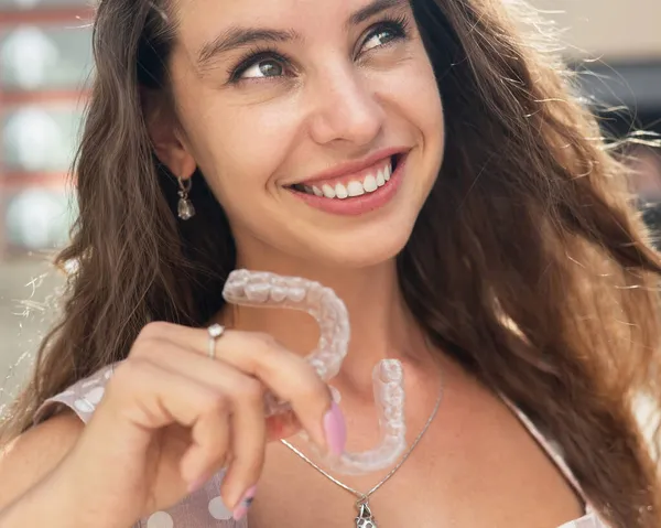 Güzel beyaz kadın ısırık düzeltmesi için şeffaf ağız koruyucuları tutuyor. Açık havada silikon telli bir kız..