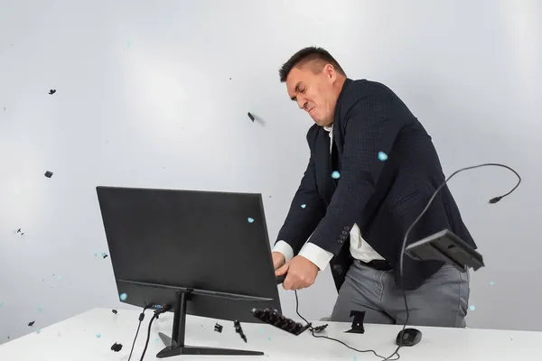 Caucásico hombre en un traje se enoja y rompe el teclado en el monitor. Un oficinista furioso rompe el ordenador. —  Fotos de Stock