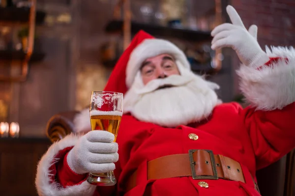 Portrét Santa Clause sedícího na kožené pohovce a pijícího k Vánocům pivo — Stock fotografie
