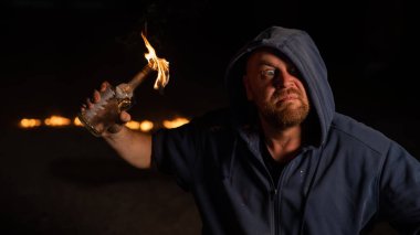 Kapüşonlu adam yanan bir şişe tutuyor. Molotof kokteyli.