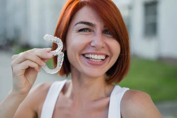 Rödhårig vit kvinna med genomskinliga tandskydd för bitkorrigering utomhus. En flicka med ett vackert snövitt leende använder silikon hängslen — Stockfoto