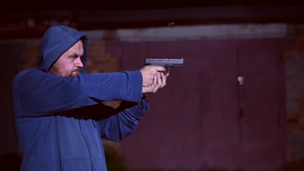 A man in a hood shoots a pistol. — Stock Video