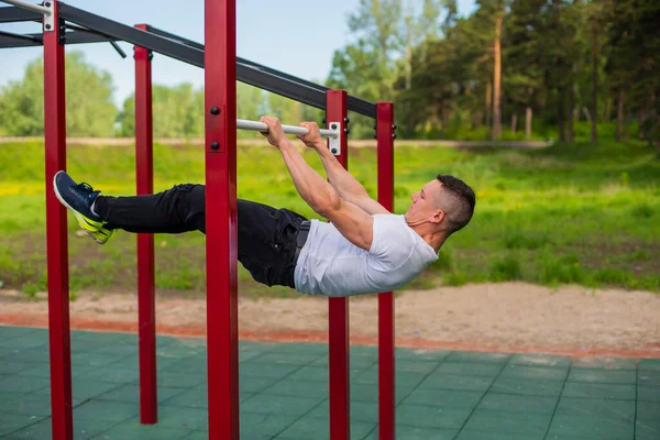 Hombre caucásico haciendo una tabla trasera en las barras irregulares. Entrenamiento en el campo de deportes. — Foto de Stock