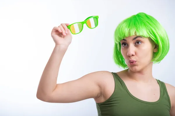 Joyeux jeune femme en perruque verte et lunettes drôles célébrant st patricks jour sur un fond blanc — Photo