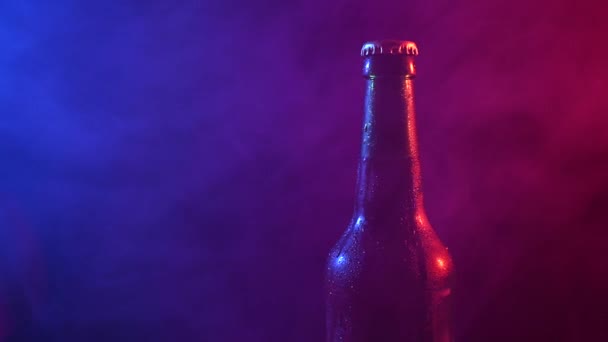 Pivní láhev se točí v modrém růžovém kouři. — Stock video