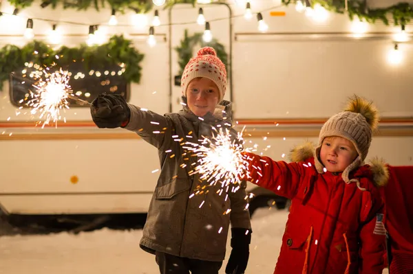 Caucasian red-haired boys hold sparklers by the trailer. Two brothers are celebrating Christmas on a trip. — Stock Photo, Image