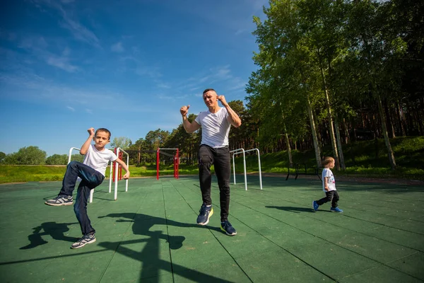 Καυκάσιος και δύο αγόρια κάνουν ασκήσεις στην ύπαιθρο. Πατέρας και γιοι εκπαιδεύονται στο γήπεδο του αθλητισμού — Φωτογραφία Αρχείου