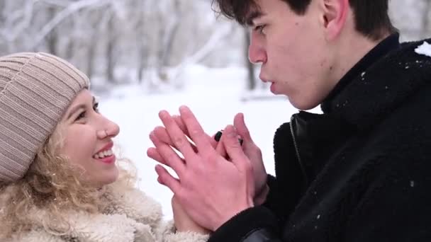 Ein junges Paar geht im Winter im Wald spazieren. Der Kerl wärmt die Hände der Mädchen. — Stockvideo