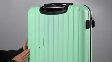 Bir kadın beyaz arka planda kırık bir bavulu gösteriyor. Uçuş sırasında hasarlı bagaj..