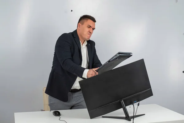 Vit man i kostym blir arg och krossar tangentbordet på skärmen. En kontorsanställd i ilska knäcker datorn. — Stockfoto