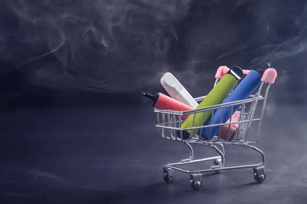 Vapores descartáveis em um carrinho de compras em um fundo preto. Modernos cigarros eletrônicos. — Fotografia de Stock