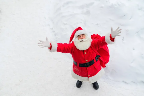 Vue de dessus sur le père noël amical claus activement geste et souhaiter joyeux Noël. Un vieil homme en costume de Père Noël se tient sur la neige dehors et souhaite une bonne année. — Photo