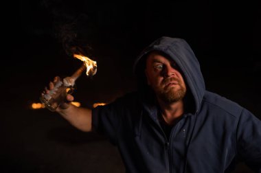 Kapüşonlu adam yanan bir şişe tutuyor. Molotof kokteyli.