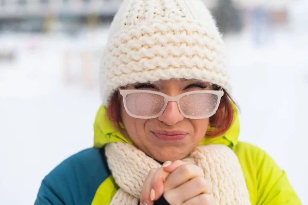 Retrato de uma mulher em óculos cobertos de geada. A menina está congelando e esqueceu luvas em tempo muito frio e sopra em suas próprias mãos — Fotografia de Stock