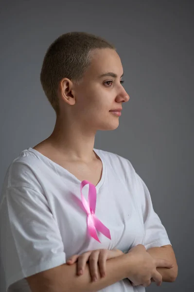 Frau mit blondem Kurzhaarschnitt mit rosa Schleife auf weißem T-Shirt als Symbol für Brustkrebs auf weißem Hintergrund. — Stockfoto