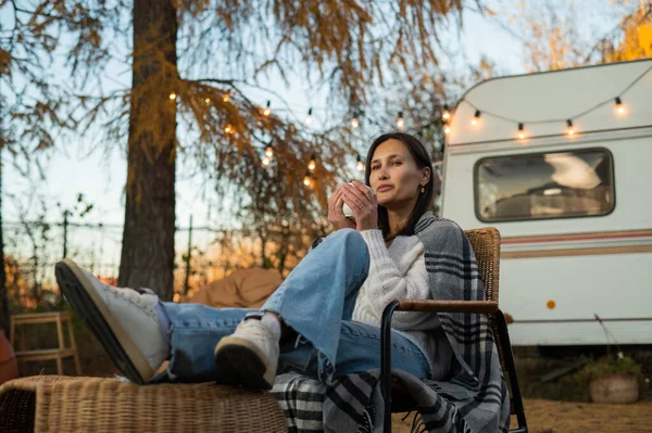 Bella donna caucasica è seduto avvolto in un plaid e bere un drink caldo all'aperto. Viaggiare in camper in autunno. — Foto Stock