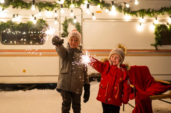 Kaukasiska rödhåriga pojkar håller tomtebloss vid husvagnen. Två bröder firar jul på en resa. — Stockfoto