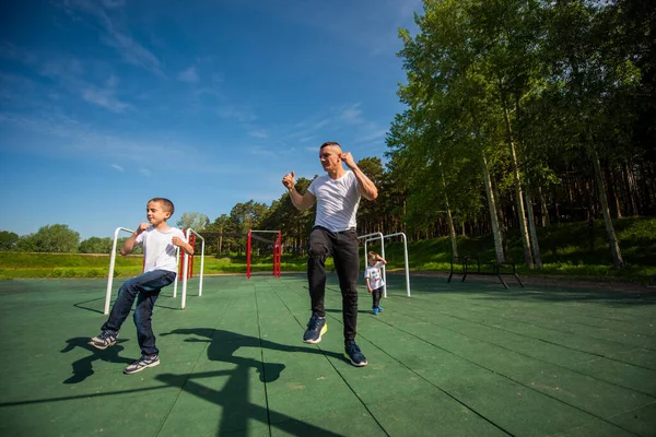 Vit man och två pojkar gör övningar utomhus. Far och söner tränar på idrottsplatsen — Stockfoto