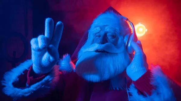 Święty Mikołaj słucha muzyki ze słuchawkami na imprezie. Niebieski czerwony neon światło i dym. — Zdjęcie stockowe