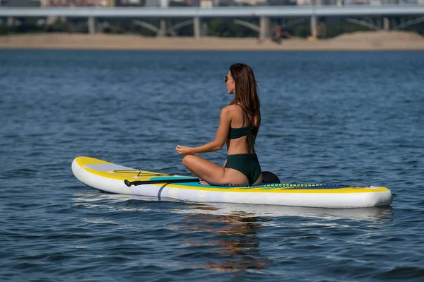 Fehér nő egy SUP táblán lovagol a folyón a városban. Nyári sport. — Stock Fotó