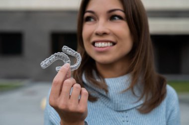 Beyaz gülüşlü, şeffaf diş teli tutan beyaz bir kadın. Isırık düzeltme aygıtı.