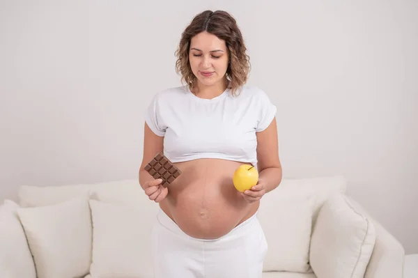 한 임산부 가사 과와 초콜릿 한 개를 들고 있습니다. 임신 9 개월째. — 스톡 사진