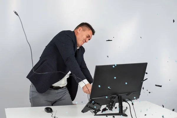 Белый мужчина в костюме злится и разбивает клавиатуру на мониторе. Работник офиса в ярости ломает компьютер. — стоковое фото