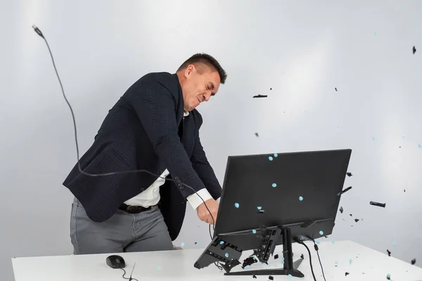 Caucásico hombre en un traje se enoja y rompe el teclado en el monitor. Un oficinista furioso rompe el ordenador. —  Fotos de Stock