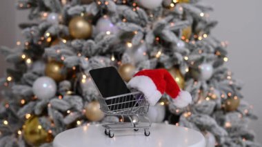 Alışveriş arabasında siyah ekranlı akıllı telefon. İnternetten Noel hediyeleri alıyorum..