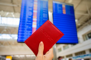 Havaalanı bilgi panosunun arka planında pasaportu olan bir kadın..