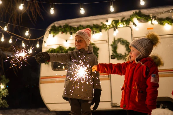 Kaukasiska rödhåriga pojkar håller tomtebloss vid husvagnen. Två bröder firar jul på en resa. — Stockfoto