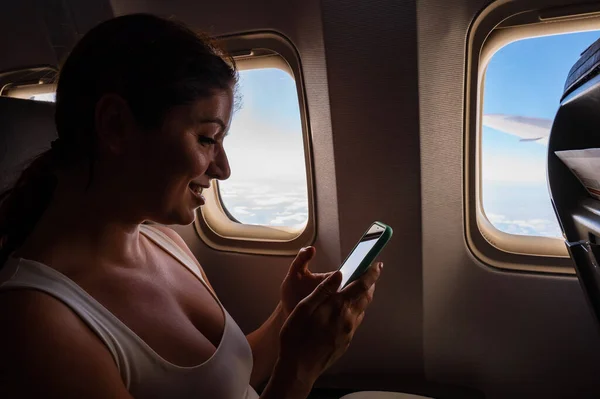 Mujer caucásica fotografías por teléfono inteligente el cielo en la ventana del avión. — Foto de Stock