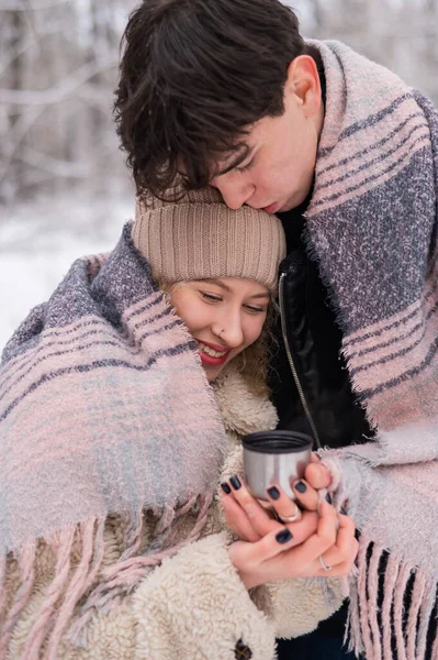 Um jovem casal caminha no parque no inverno. O tipo e a rapariga estão a beber uma bebida quente ao ar livre.. — Fotografia de Stock