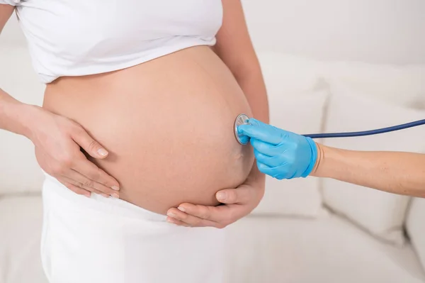 医師は妊娠中の女性の腹の中に心臓の音を聴きます. — ストック写真