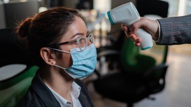 Doktor bir ofis çalışanının ısısını kızılötesi termometreyle ölçer.. 