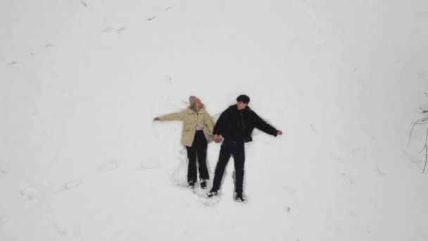 Vista superior de un chico y una chica haciendo ángeles en la nieve. — Vídeo de stock