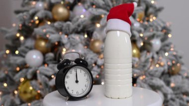 Noel Baba şapkalı bir şişe süt ve bir Noel ağacının arka planında çalar saat. Noel Baba için ikramlar.