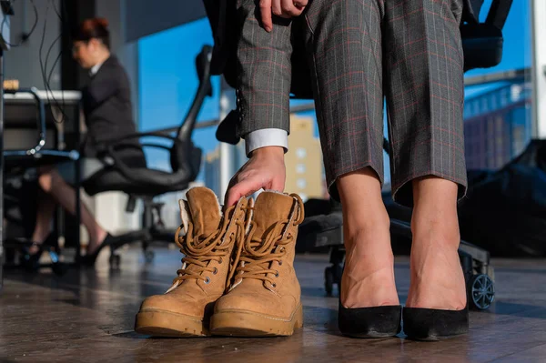Επιχειρηματίας αλλάζει παπούτσια με ψηλά τακούνια σε μπότες στο γραφείο. Τέλος της εργάσιμης ημέρας. Κουρασμένα πόδια — Φωτογραφία Αρχείου