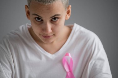 Kısa sarı saçlı, beyaz tişörtlü, pembe kurdeleli, beyaz arka planda göğüs kanserinin sembolü olan bir kadın..